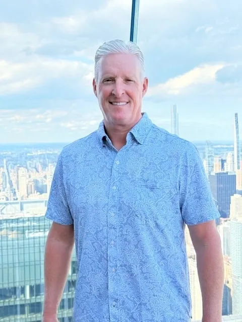 Man in blue shirt, city skyline background.